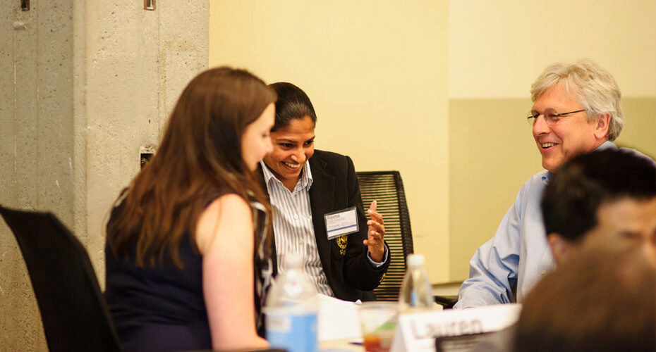 A small group of people engaged in a lively discussion or meeting around a table. They appear to be interacting in a professional or academic setting.