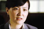 Headshot of a person with short dark hair, wearing a suit jacket and earrings, looking to the side with a neutral expression.