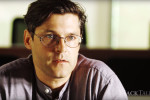 A headshot of a person wearing glasses, looking intently ahead with a slight expression of concentration or thoughtfulness. The background is blurred.