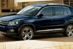 A dark blue Volkswagen SUV parked on a street in an urban setting. The vehicle is facing left with sunlight reflecting on its surface.