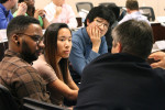 A group of people engaged in discussion in a conference room setting, sitting around a table with focus on attentive conversation.