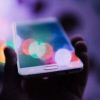 A hand holding a smartphone with a colorful, blurred bokeh effect in the background, representing technology and digital connectivity.