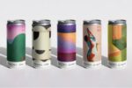 Five beverage cans with artistic labels featuring various abstract and colorful designs are standing in a row.