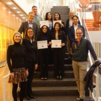 A group of people standing on stairs in a modern building. Three individuals hold certificates labeled "Y-Prize Winners." The setting appears formal.